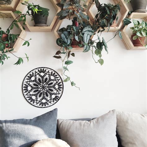 Záber na detailnú drevenú mandalu zavesenú na stene v svetlom, minimalistickom interiéri